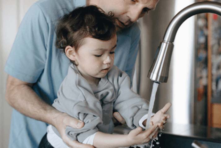 Man helping little boy wash his hands under a sink